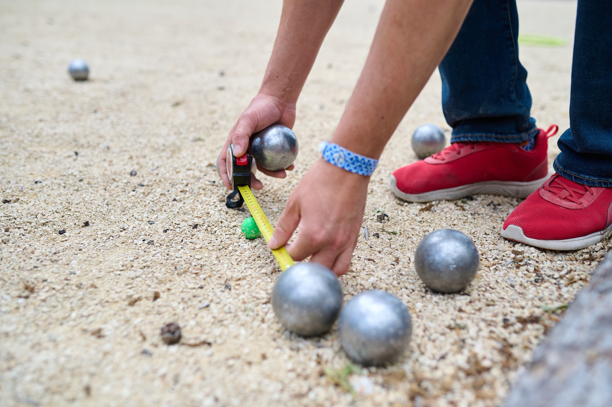 A player measures the distance between boules and the jack on a petanque court